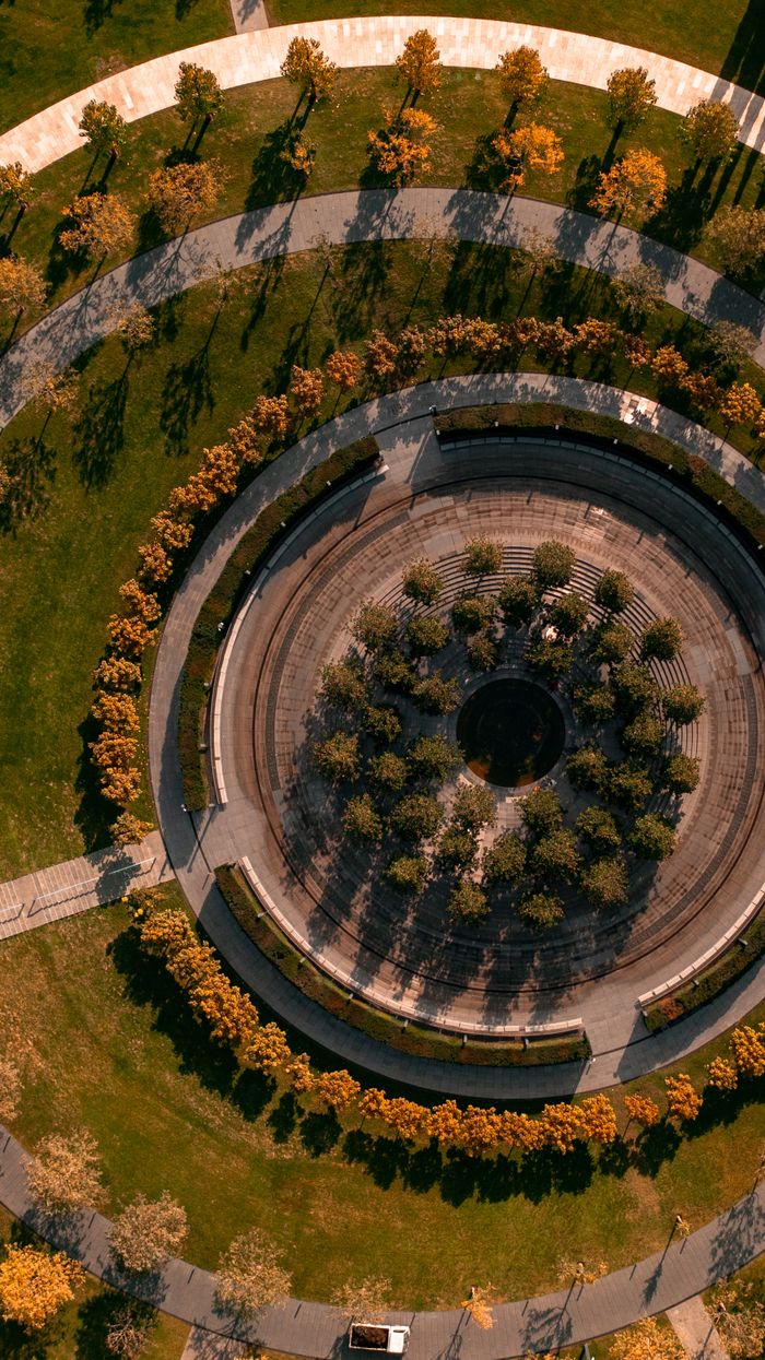 Aerial shot of a landscaped circular garden with concentric pathways and autumn foliage.
